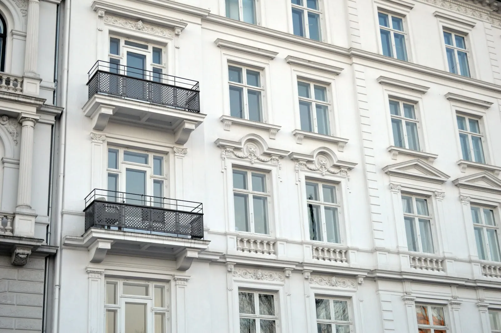 Façade classique blanche avec des balcons en fer forgé et de hautes fenêtres.