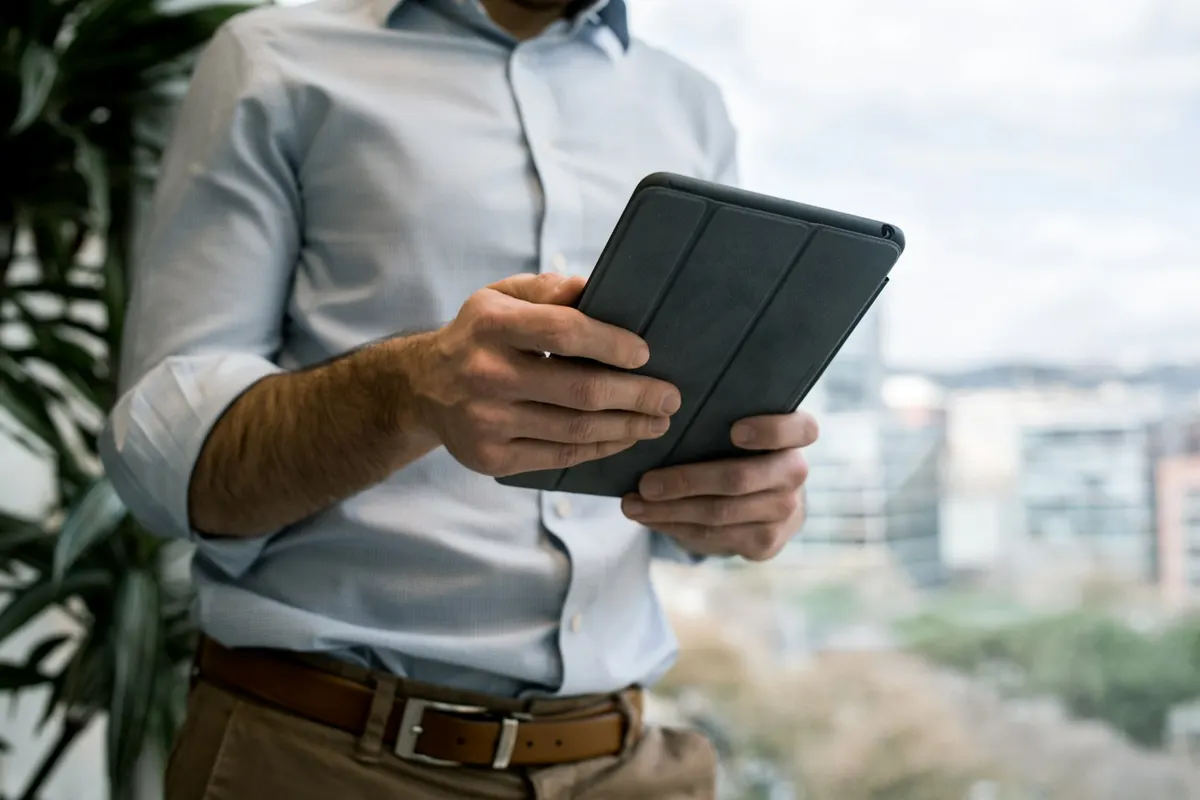 Professionnel près d'une baie vitrée consultant une tablette.